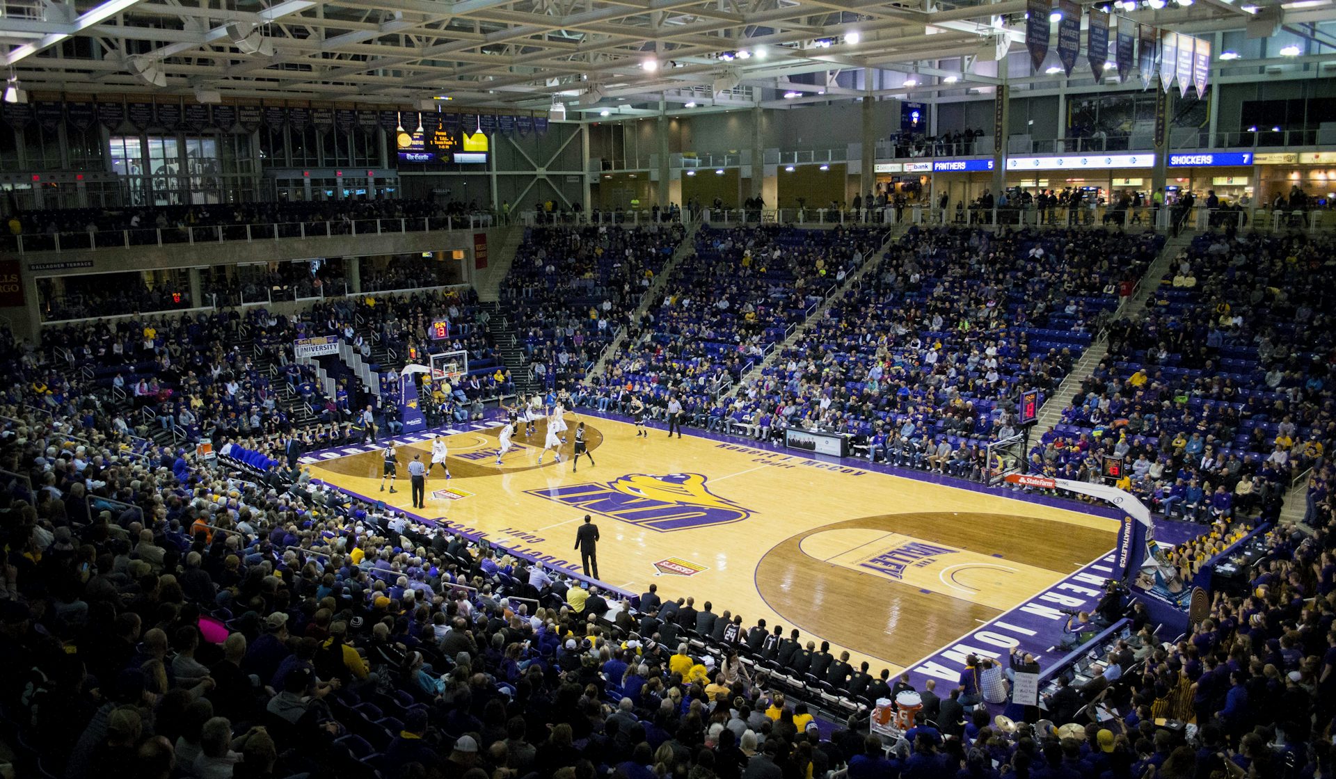 A full basketball arena seen from the stands, the crowd surrounding the court