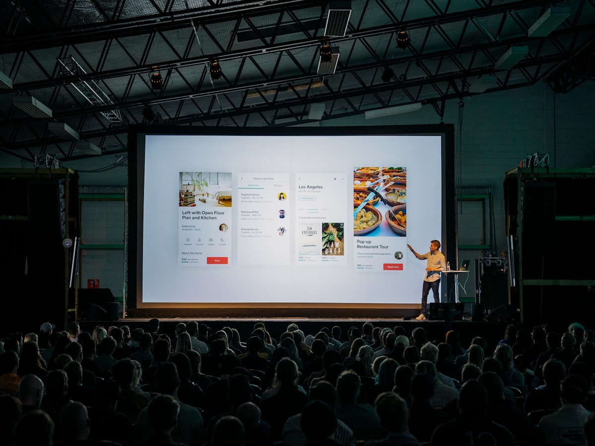 A speaker presenting in front of a large screen in a dim room